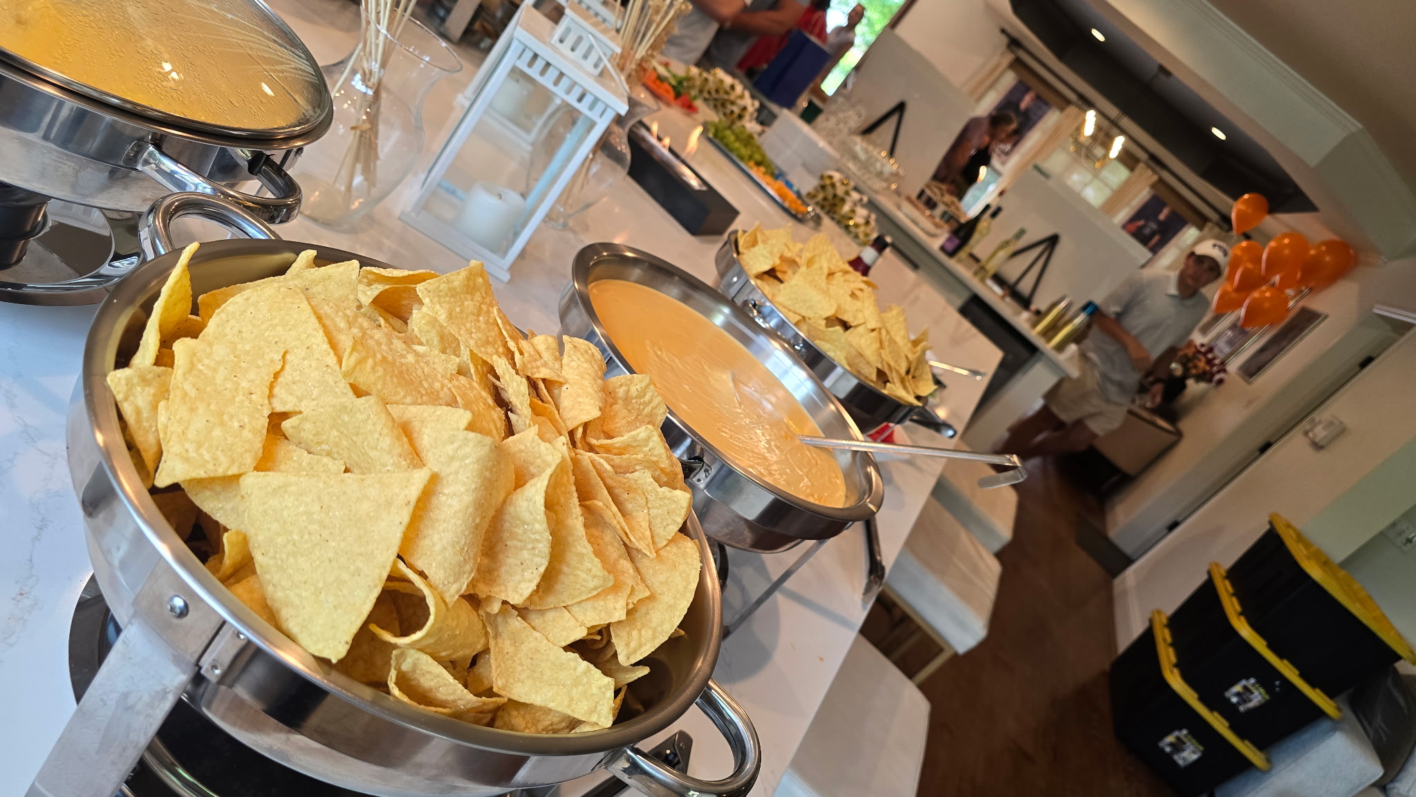Loaded nacho bar buffet setup with tortilla chips, house queso, and toppings for a backyard catering event